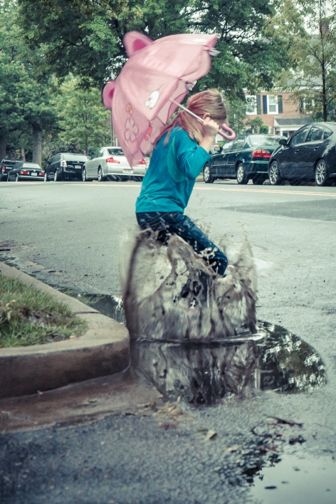 girl jumps in a puddle while holding an umbrella in the rain NotSoSAHM
